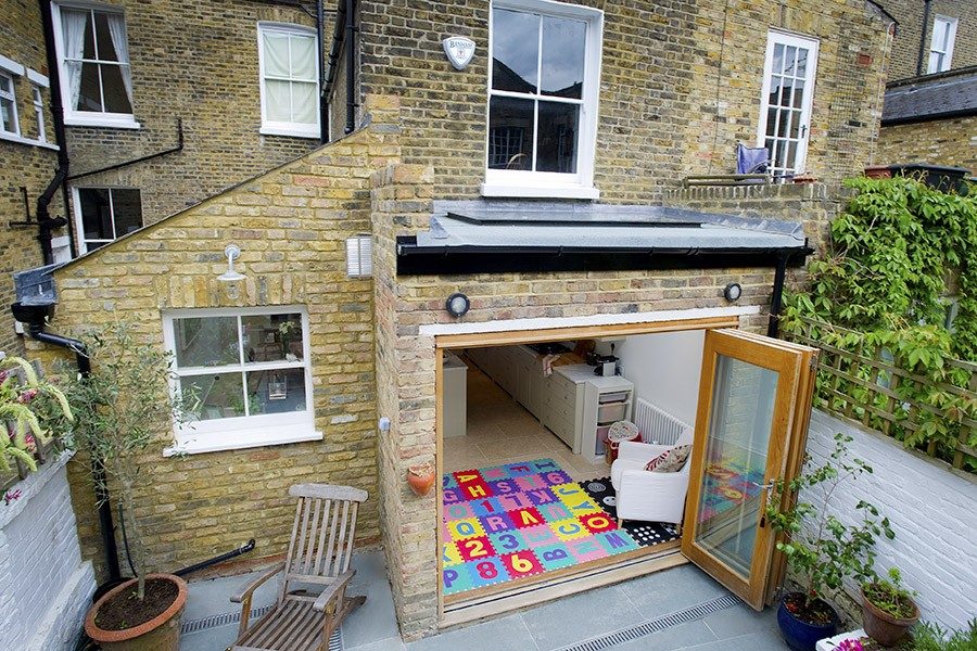 Small flat-roof rear extension on a London brick terrace with bifold doors open to a patio, a Build Team project