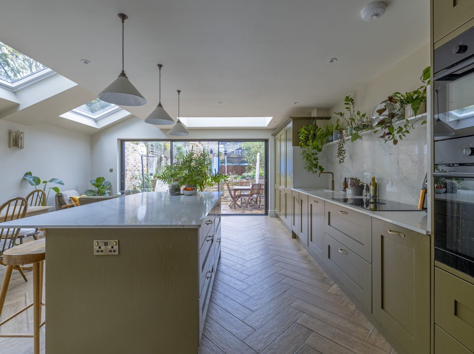 Central kitchen island with white marble worktop and green cabinetry at Mayfield Road N8
