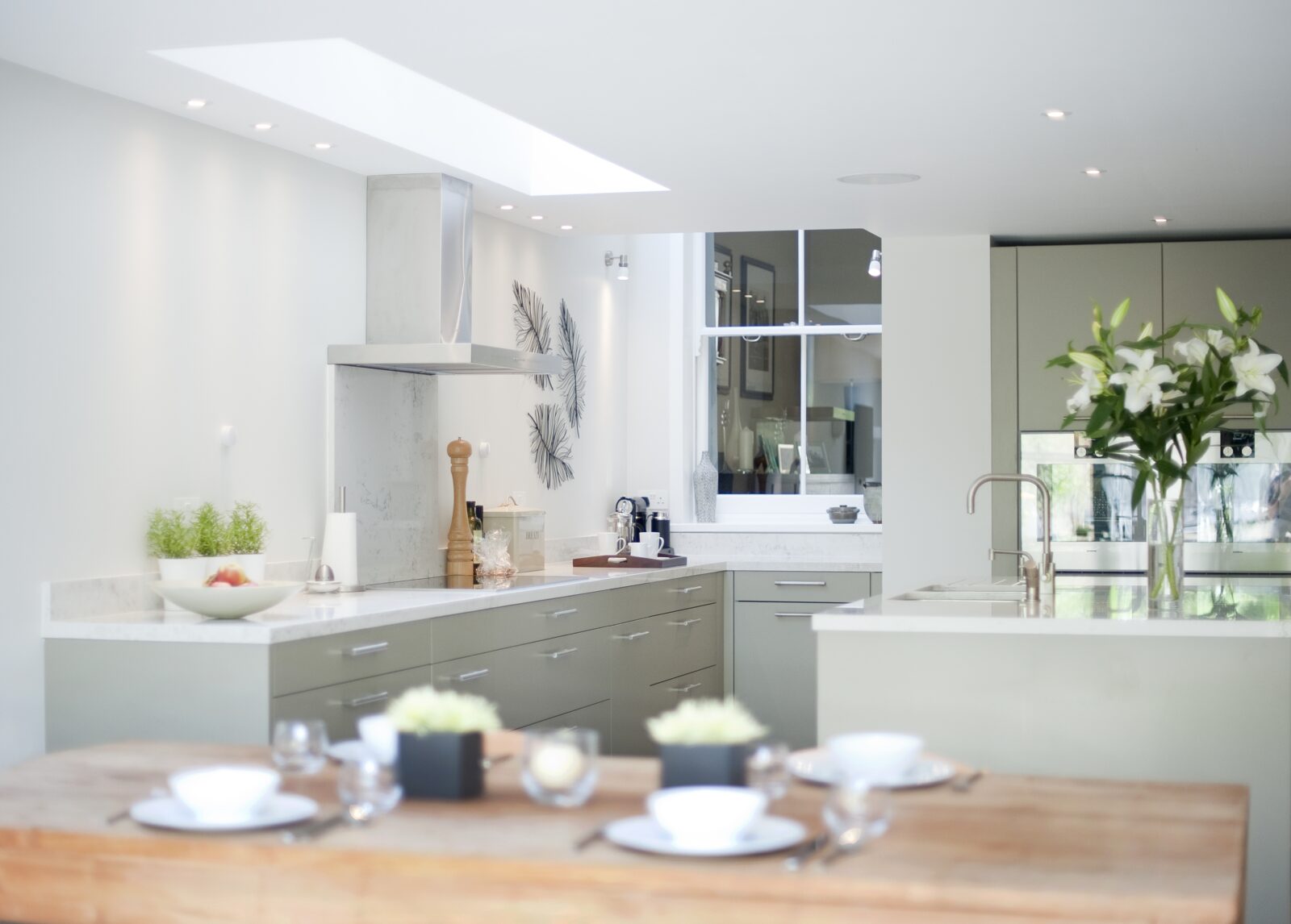 Kitchen extension with a long rooflight and sage green units, with a white-framed window in the back wall looking into the room behind